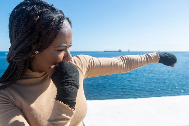 Jeune fille noire afro formation arts martiaux, boxe en plein air avec mer et ciel bleu