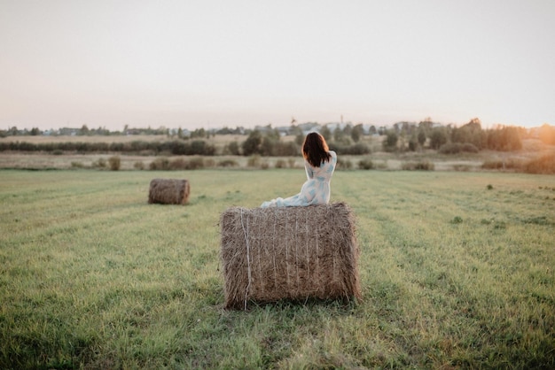 jeune fille nue avec un cul sexy est assise sur une botte de foin dans un champ en été Ajout de l'effet d'un petit grain de film