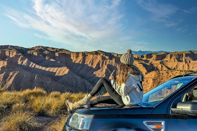 Jeune fille observant le paysage désertique perché sur le capot d'une voiture