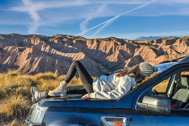 Jeune fille observant le paysage désertique perché sur le capot d'une voiture