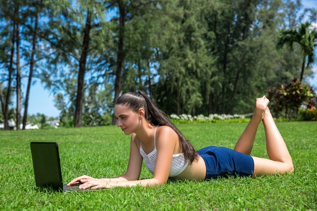 Jeune fille avec un ordinateur portable assis sur l'herbe dans le parc