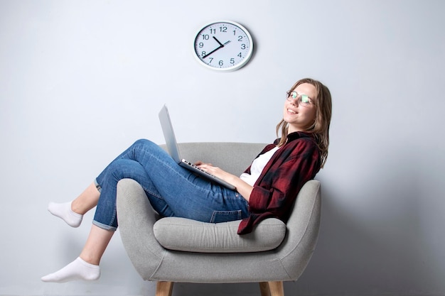 Jeune fille avec un ordinateur portable assise sur une chaise douce et confortable et faisant des heures supplémentaires