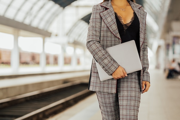 Jeune fille avec ordinateur portable fermé dans les mains debout dans la gare urbaine