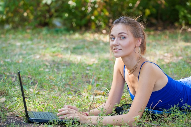 Jeune fille avec un ordinateur portable sur l'herbe dans le parc