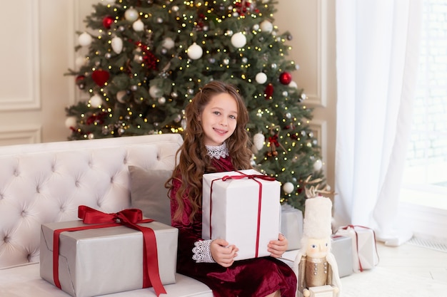 Jeune fille ouvre un grand cadeau de Noël dans le salon, la fille tient un cadeau de Noël.