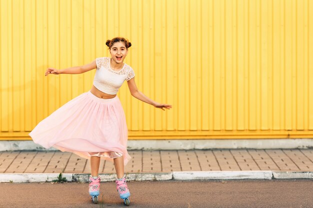 Jeune fille en patin à roues alignées sur mur jaune