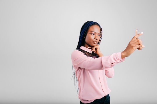 Jeune fille à la peau sombre prenant selfie en studio blanc