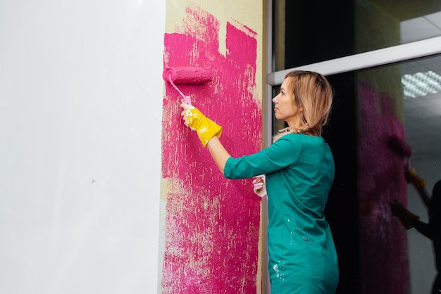 Une jeune fille peint un mur avec un rouleau en rose dans son nouvel appartement Rénovation de l'intérieur et d'un nouvel appartement Pendaison de crémaillère et hypothèque souhaitable