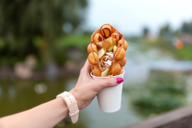 La jeune fille pendant la promenade tient dans sa main un gobelet en papier avec une gaufre belge sur un parc verdoyant