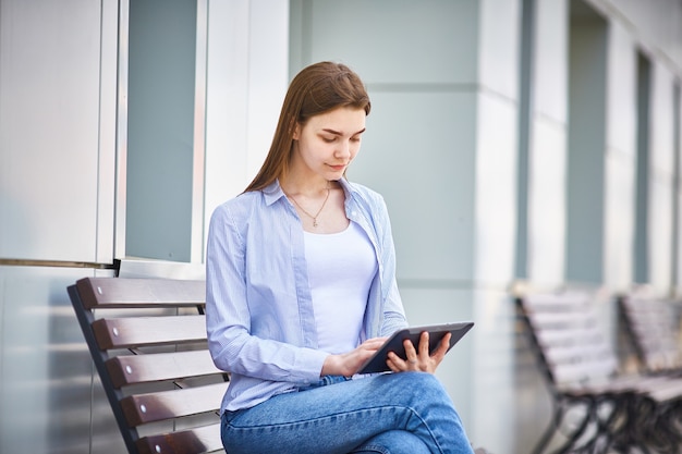 Jeune fille pensive, assis sur un banc avec une tablette dans la main.