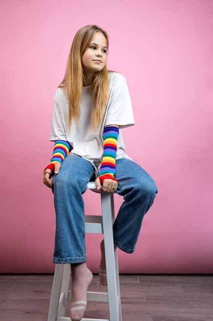 Une jeune fille pensive est assise sur une chaise blanche sur fond rose