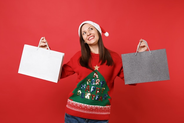 Jeune fille pensive de Santa recherchant, tenant des sacs de paquets avec des achats après le shopping isolé sur fond rouge vif. Bonne année 2019 concept de fête de vacances célébration. Maquette de l'espace de copie.