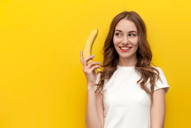 jeune fille pensive tenant une banane et souriant sur un fond jaune isolé femme rêve