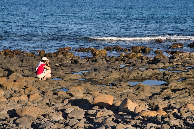 Jeune fille photographiant la plage de terrain accidenté formée par des roches volcaniques provenant du refroidissement de la lave