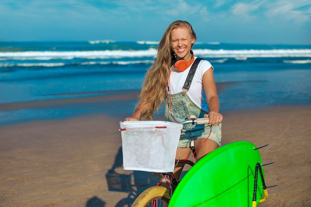 Jeune fille avec planche de surf et vélo sur la plage