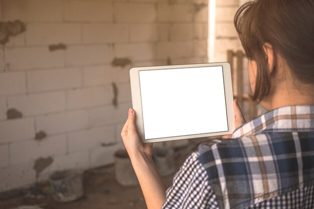 Une jeune fille planifie la construction et la rénovation d'un concept de maison, une maquette d'écran de tablette avec un écran blanc vierge à la main, une photo de l'espace de copie
