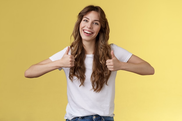 Une jeune fille pleine de vie et confiante, positive et sortante, soutient une longue coupe de cheveux bouclés, un grand effort, une réponse positive approuvant un bon choix, comme votre tenue souriante sur fond jaune. Mode de vie.