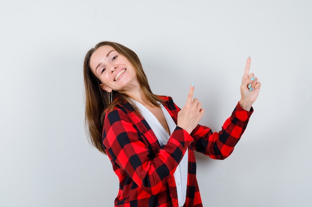 Jeune fille pointant vers le haut, debout sur le côté en chemise à carreaux, chemisier et l'air heureux.