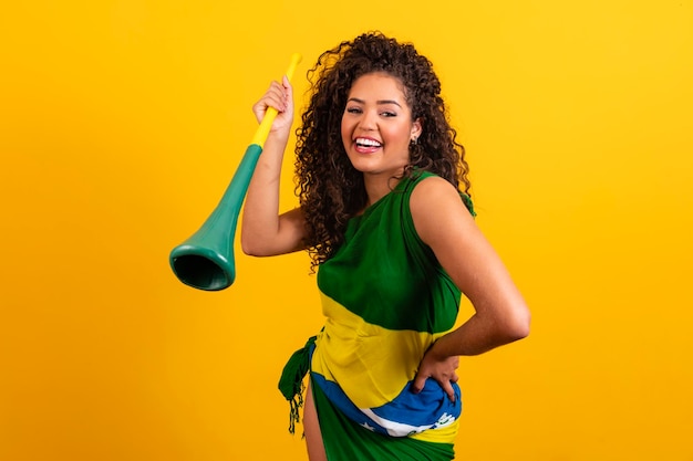 Jeune fille pom-pom girl brésilienne avec une vuvuzela sur fond jaune célébrant