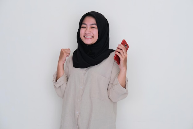 Jeune fille portant le hijab souriante excitée tout en tenant son téléphone portable