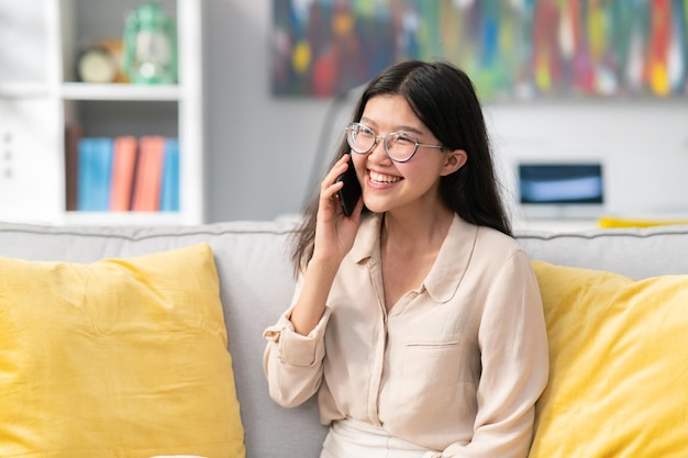 Une jeune fille portant des lunettes est assise sur le canapé dans la chambre et appelle le meilleur ami, ils parlent au téléphone