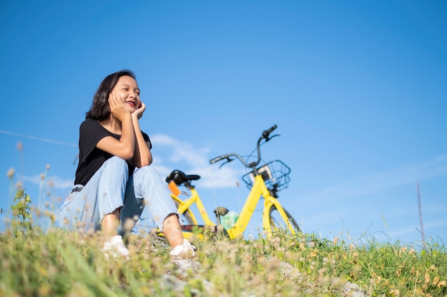 Jeune fille portant un T-shirt noir jean assis avec vélo au parc avec ciel bleu