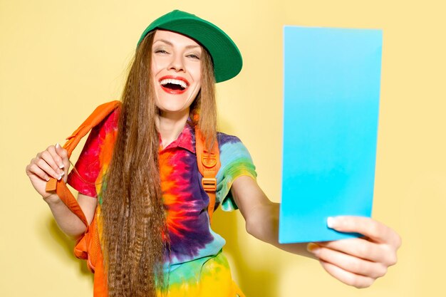 jeune fille portant des vêtements lumineux tenant une carte bleue et un sac à dos sur jaune