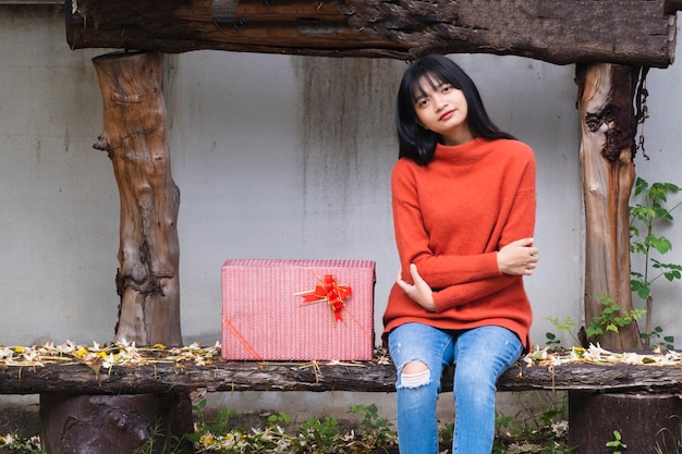 Une jeune fille porte un pull orange assis sous l'arbre avec une boîte-cadeau.