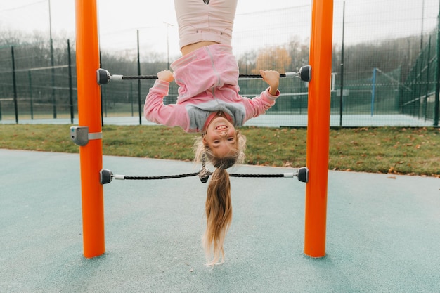 Une jeune fille sur un portique est suspendue à l'envers sur une aire de jeux pour enfants.