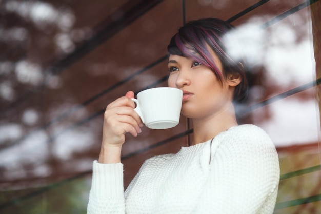 Jeune fille posant avec du café derrière la fenêtre