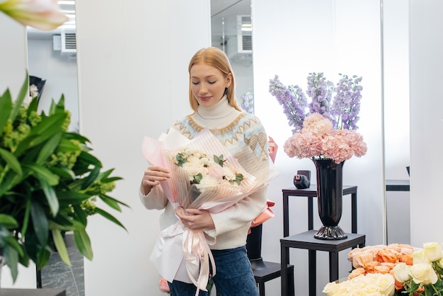 Une jeune fille pose avec un beau bouquet festif dans le contexte d'un magasin de fleurs confortable Fleuristerie et confection de bouquets dans un magasin de fleurs Petite entreprise