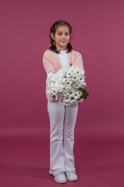 Une jeune fille pose sur un fond rose avec des fleurs dans ses mains chrysanthème