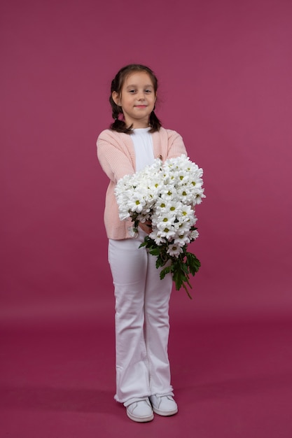 Une jeune fille pose sur un fond rose avec des fleurs dans ses mains chrysanthème