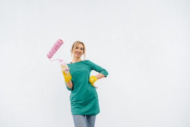 Une jeune fille pose avec un rouleau devant un mur blanc. Réparation de l'intérieur.