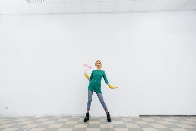 Photo une jeune fille pose avec un rouleau devant un mur blanc. réparation de l'intérieur.