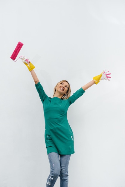 Une jeune fille pose avec un rouleau rose avant de peindre un mur blanc. Réparation de l'intérieur.