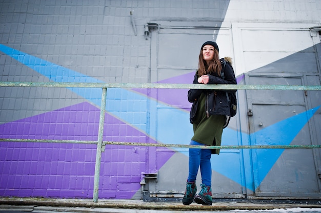Photo jeune fille posée contre un mur coloré dans une journée froide.