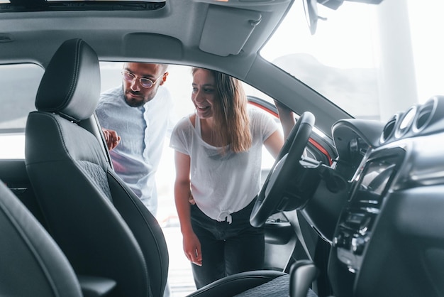 Une jeune fille positive rend visite à un salon de l'auto et choisit un gestionnaire de voiture pour l'aider