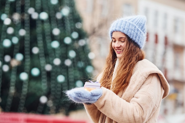 Une jeune fille positive tient une petite boîte-cadeau dans les mains à l'extérieur de la ville.