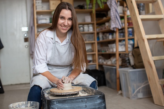 Une jeune fille potière, assise dans un atelier de céramique derrière un tour de potier