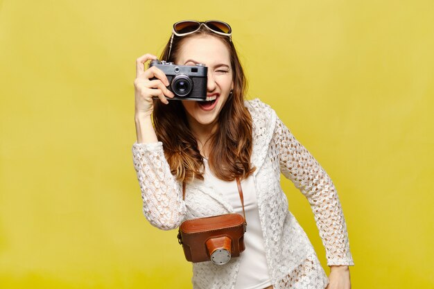 Une jeune fille prend des photos avec un appareil photo rétro sur un fond jaune.