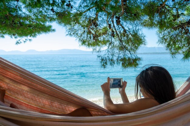 Jeune fille, prendre photo, à, a, smartphone, mensonge, dans, a, hamac, plage