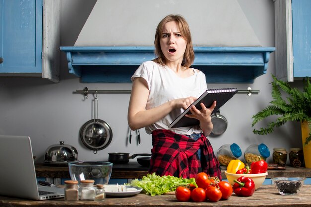 Une jeune fille prépare une salade végétarienne dans la cuisine et se penche sur un livre de recettes qu'elle apprend à cuisiner