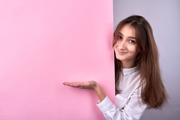 Jeune fille présentant un espace de copie sur un mur rose