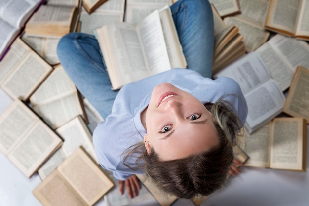 Une jeune fille en pull bleu et jeans est assise sur une pile de livres Éducation et étude Vue de dessus