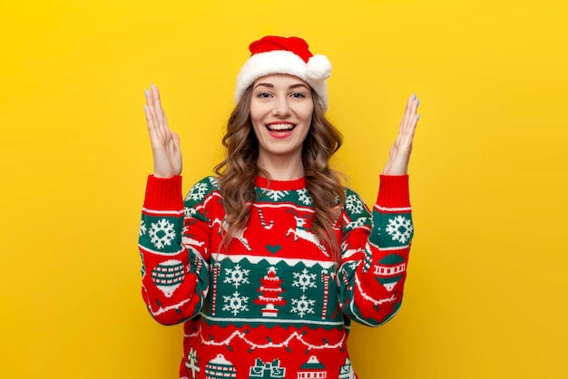 une jeune fille en pull de Noël et chapeau de père Noël tient les mains vides devant elle