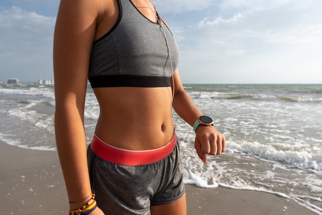 Jeune fille qui court sur la plage et regarde sa montre avec un short et un haut