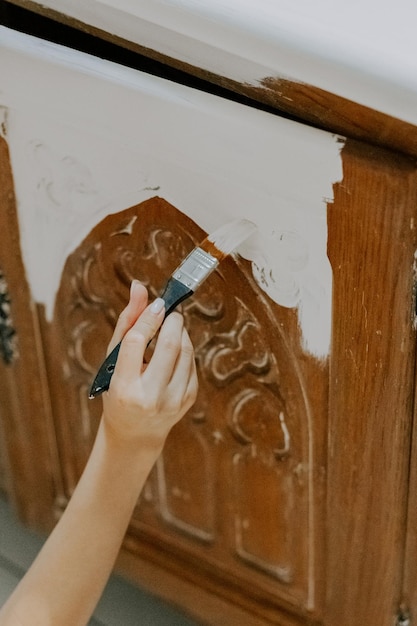 Une jeune fille de race blanche peint la porte à motifs d'une vieille armoire rétro dans sa chambre avec un pinceau