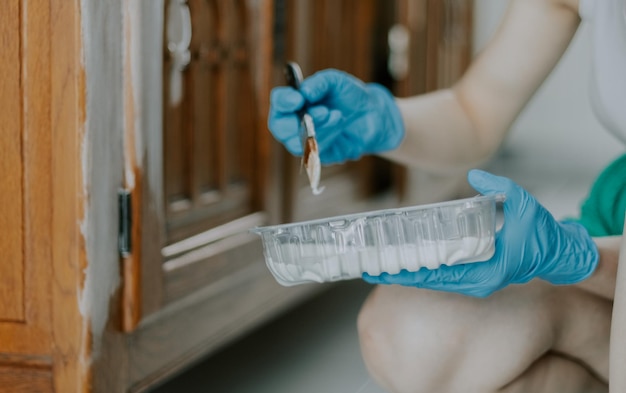 Une jeune fille de race blanche tient une boîte transparente de peinture blanche et peint le meuble