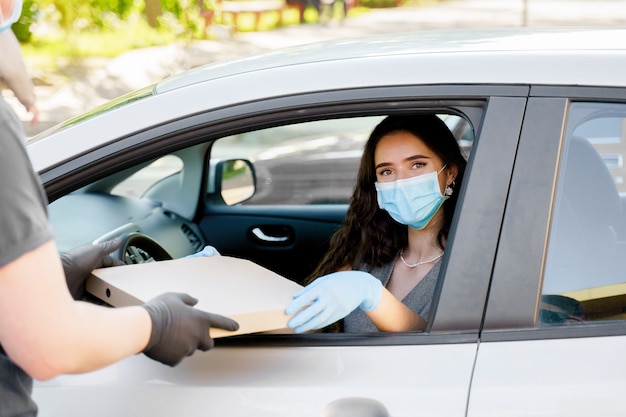 Jeune fille reçoit une boîte à pizza en voiture avec un masque médical et des gants